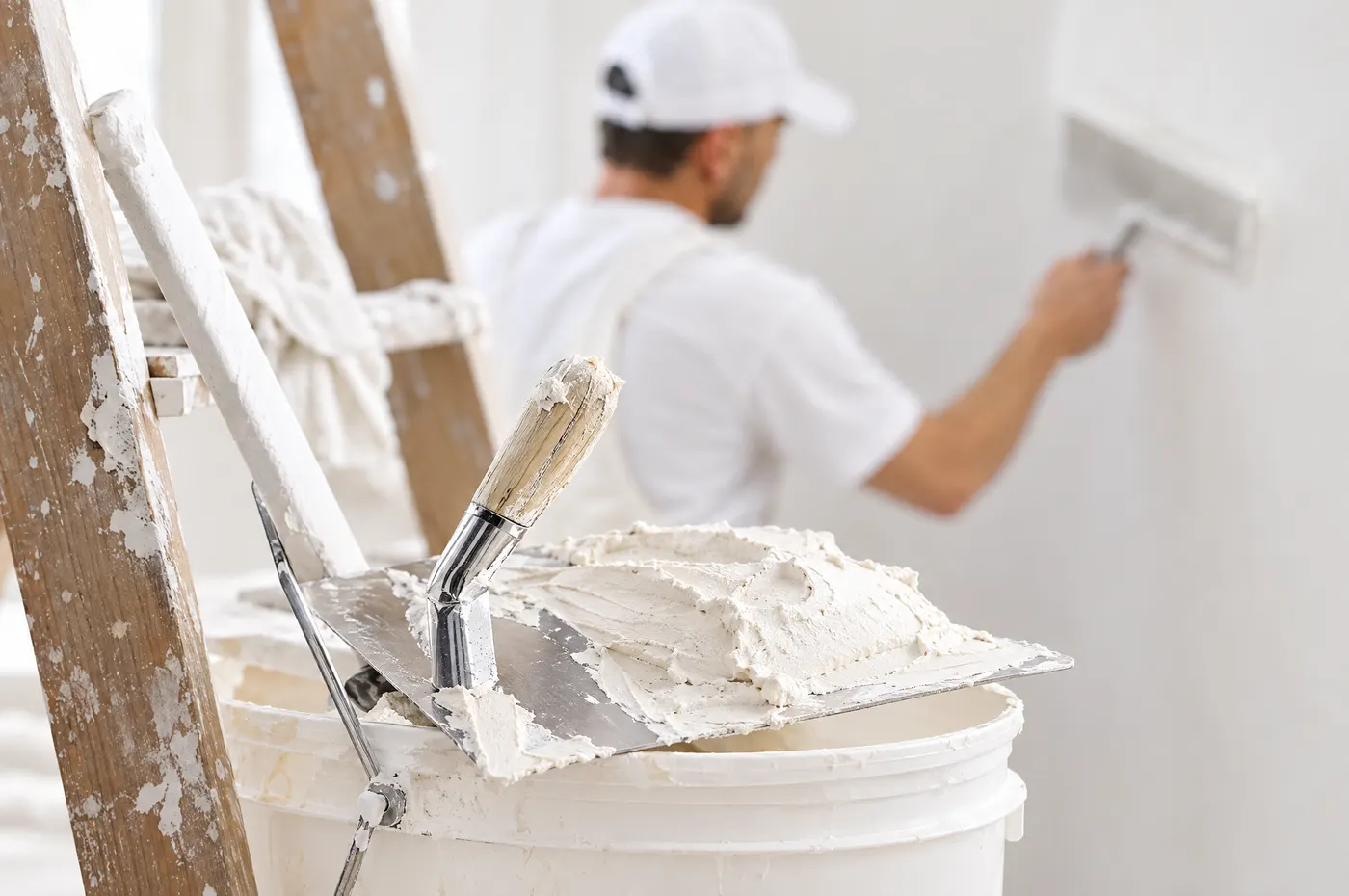 Glättekelle mit frischem Weissputz, dahinter ein Gipser beim Verputzen einer Wand