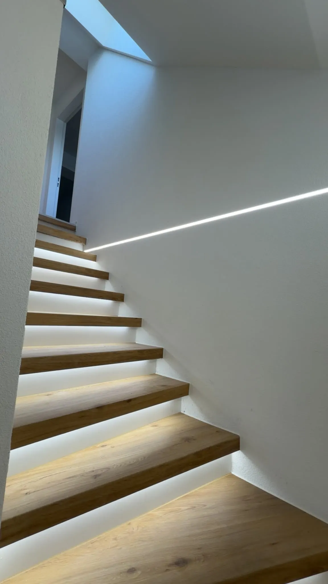 Treppe mit Eichenstufen, weisser Wand und Lichtband